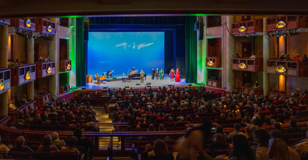 wide shot of a crowded theater with a play happening on stage